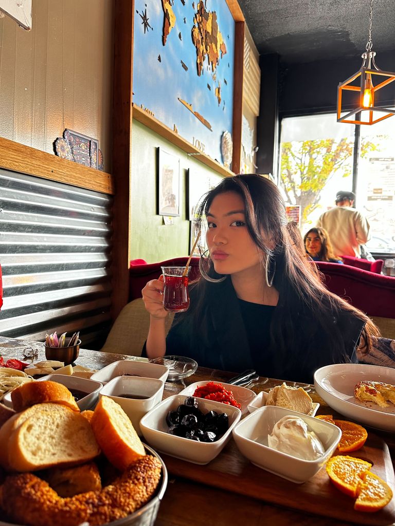 Boston University student Robin Kim (COM'24, CAS'24). She is sitting at a cafe with breakfast food in front of her while sipping on a tea.