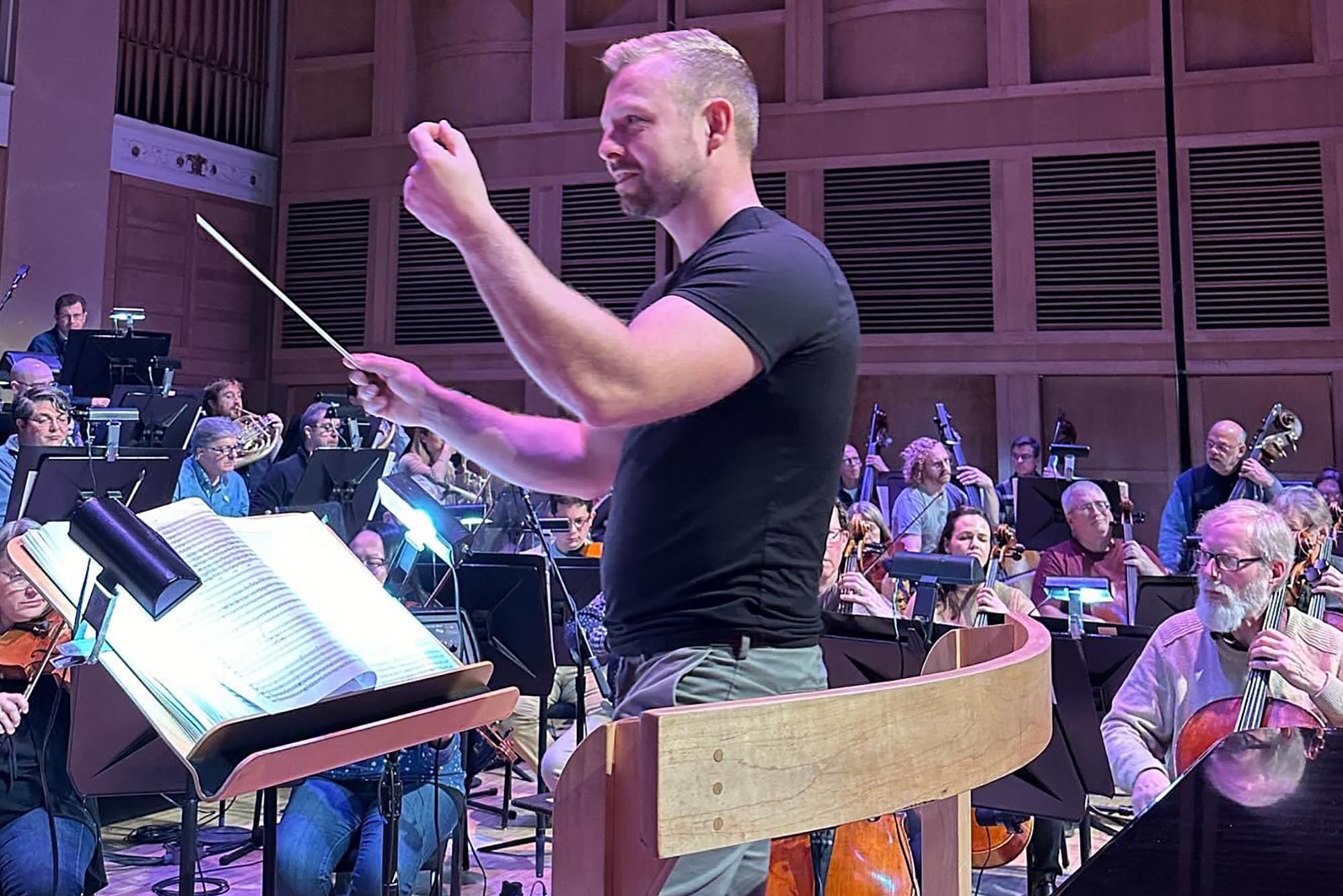 Photo: Daniel Parsley in a black tshirt and gray slacks, converses with the members he is conducting in a rehearsal.
