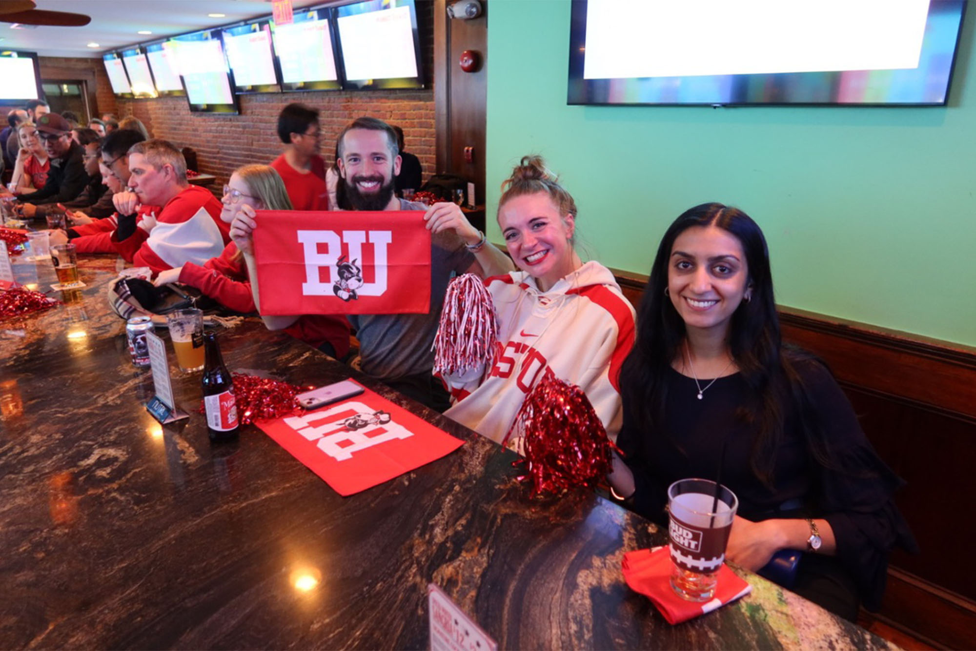 Photo: Students at a watch party in DC wear red and white Boston University hockey gear for the Men's beanpot semifinal game