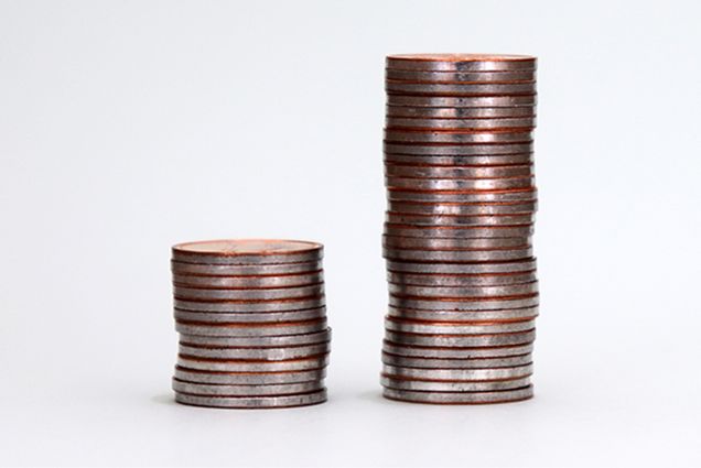 Photo: Two stacks of coins, one large and one small. Depicts wealth inequality