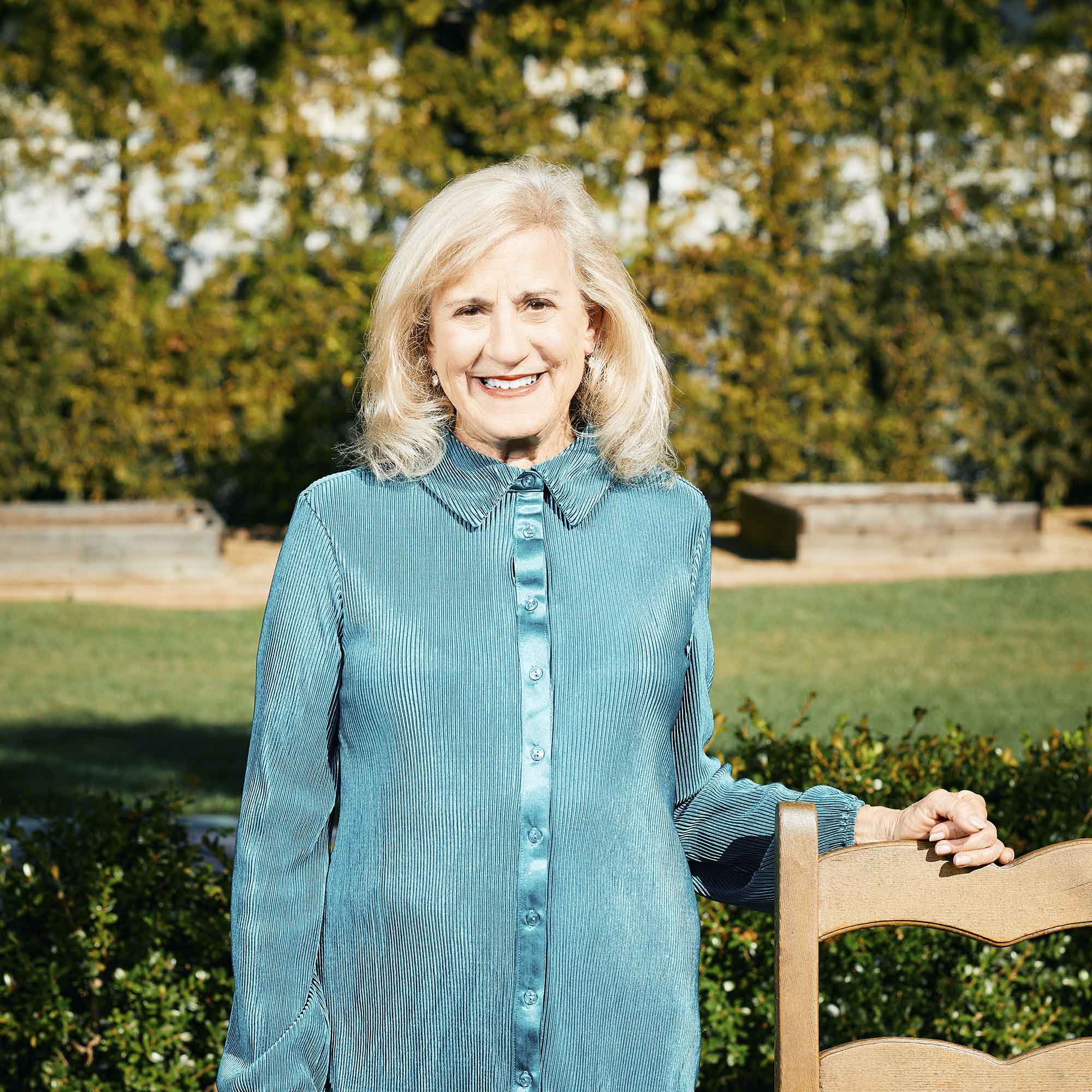 Photo: A white woman with a teal button up and teal slacks poses for a photo. She smiles for the photo with her blonde hair.