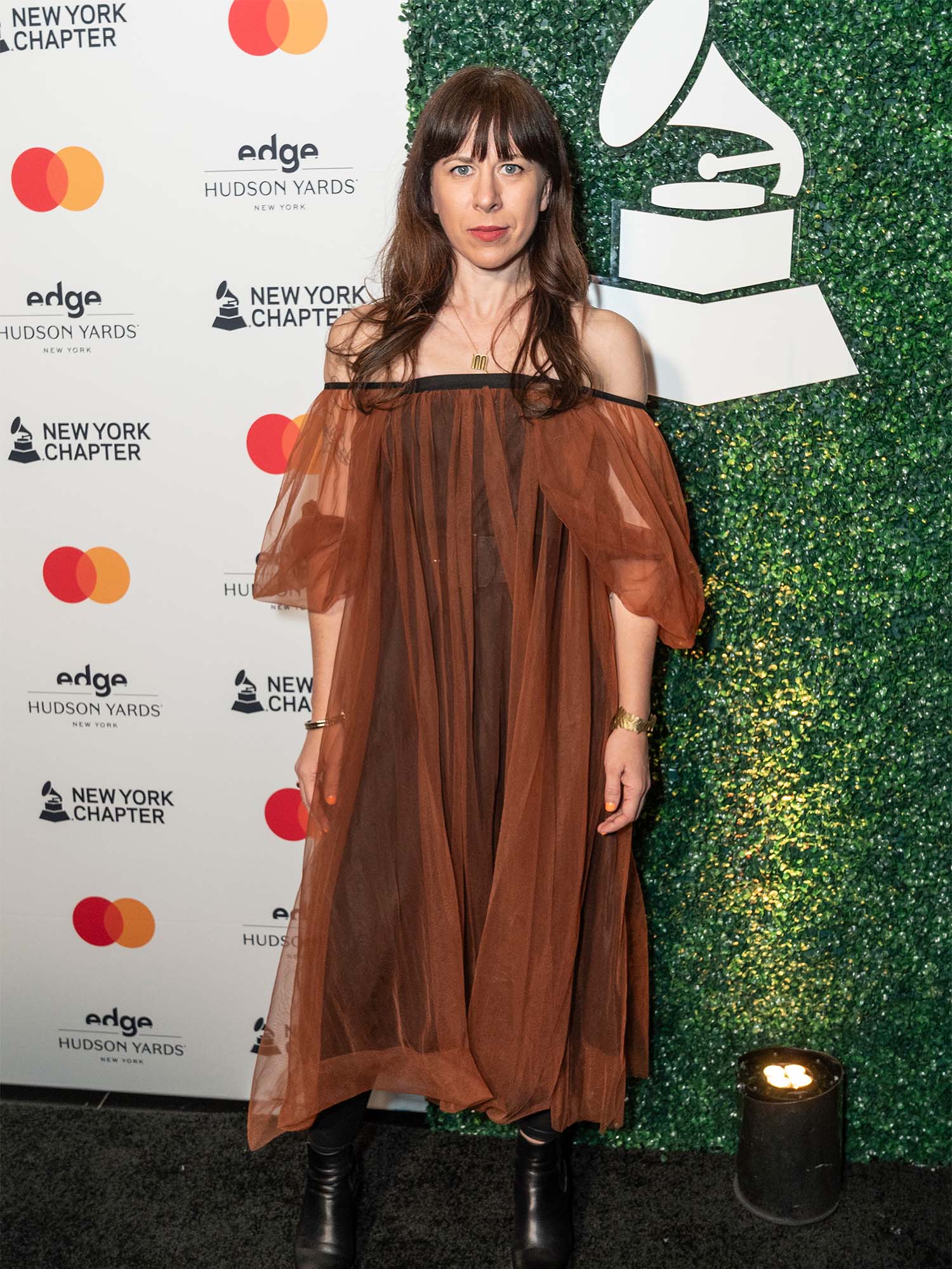 Photo: A woman in an elegant flowing dress stands in front of a photoboard at the 2024 Grammys