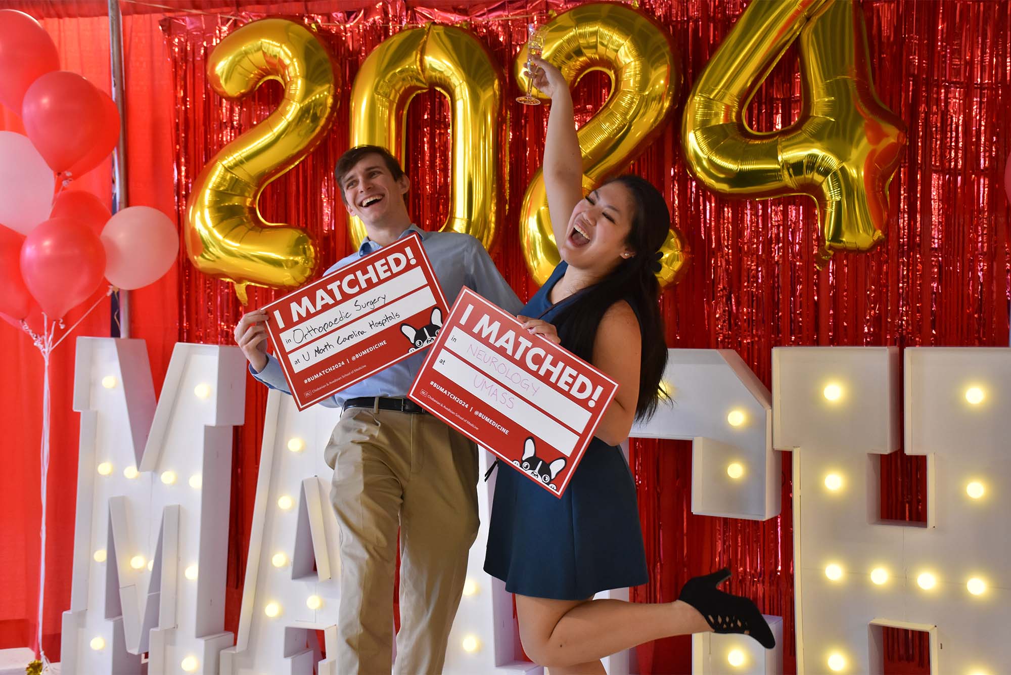 Photo: A couple of people in formal attire holding up signs that say "I Matched!" in front of a red background