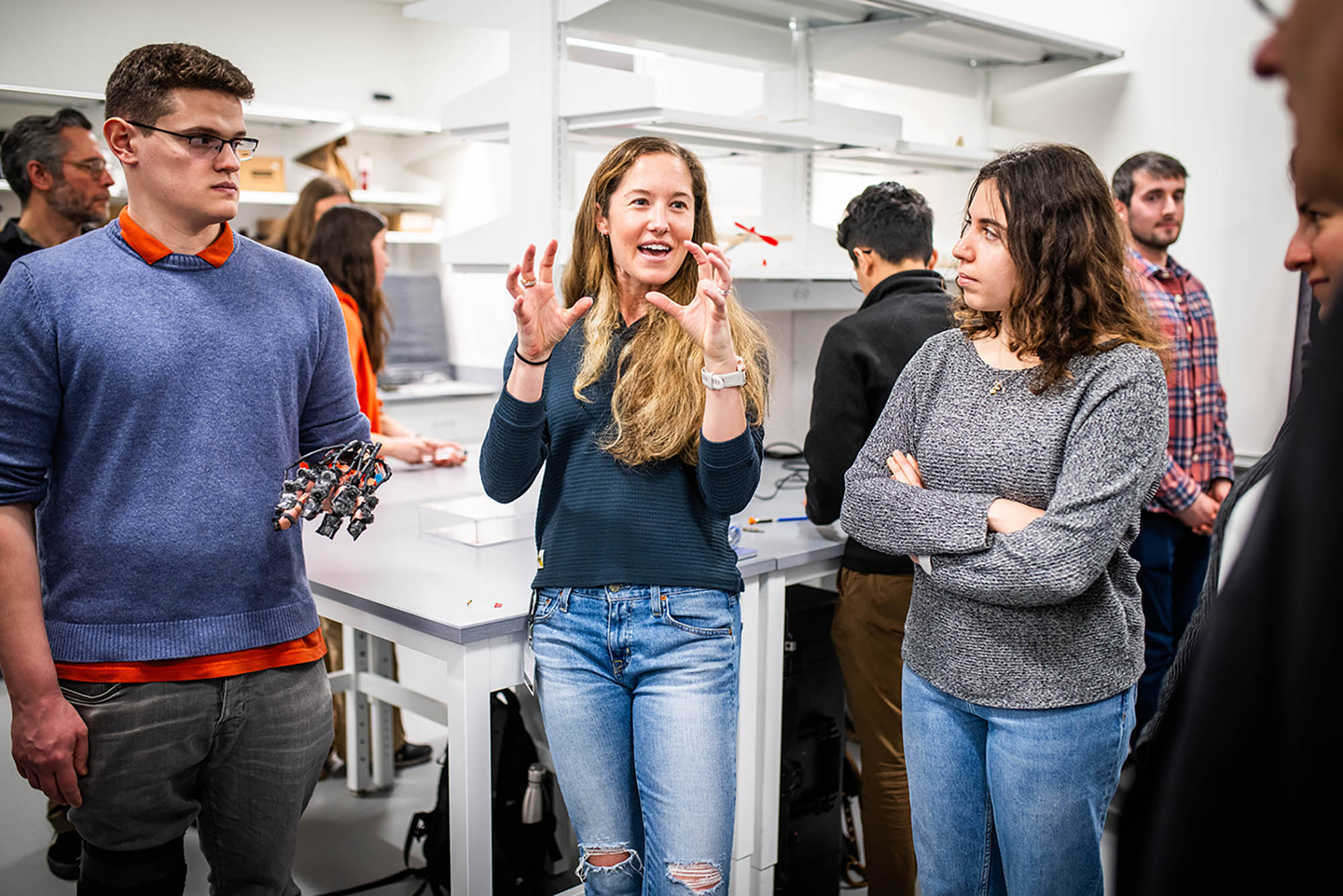 Photo: Engineering PhD students, Lorenzo Kinnicutt (left) (ENG 25) , Leah Gaeta (ENG 25) and Meliha Albayrak (ENG 26) demonstrate a robotic hand used in rehabilitation during the opening of the College of Engineering's new RASTIC event. They stand in a sterile place.
