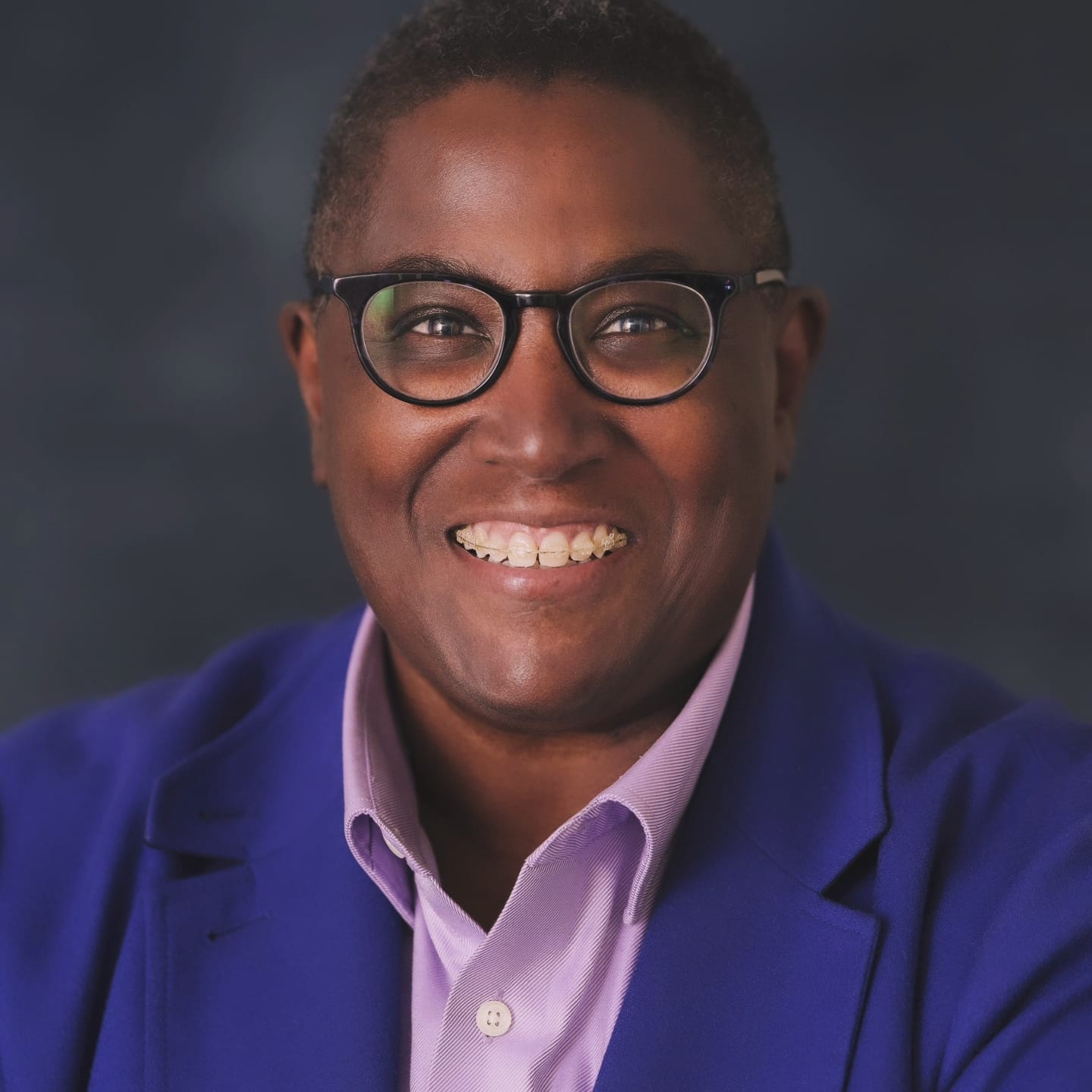Photo: Judi Burgess, a Black woman wearing glasses with a pink shirt and blue jacket blazer, poses for a photo. She is the director of Labor Relations for BU and co-director of BU's LGBTQIA task force.