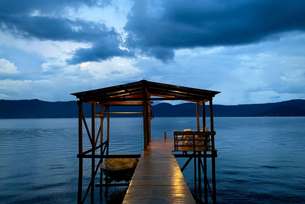 Photo: A shot of a dock at dusk, with the clouds in the sky and a faint light on the wooden pathway up to the dock.