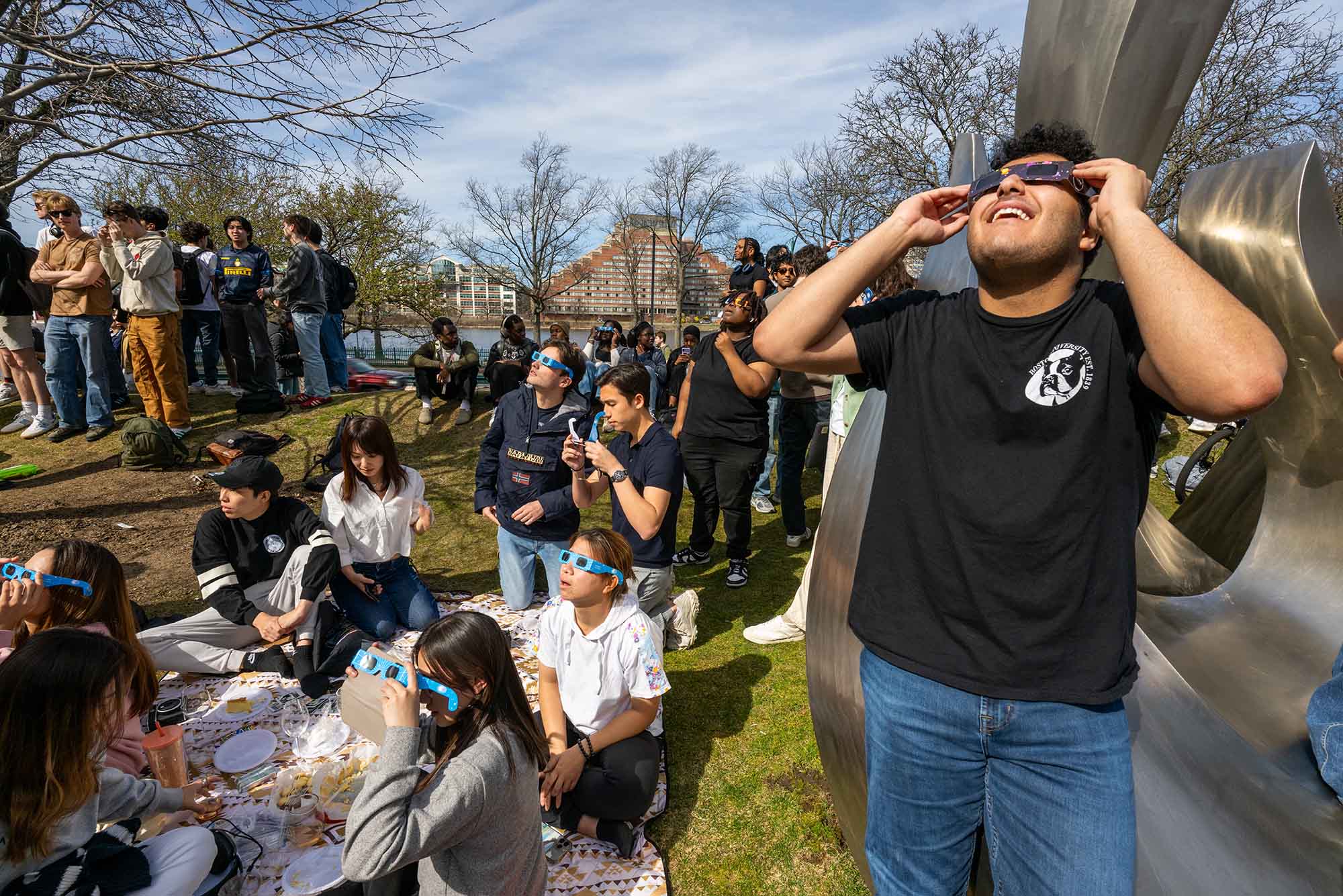 Photo: Surrounded by crowds with the same plan, Tawfiq Mukahall (Questrom’27) takes int he eclipse with a pair eclipse glasses on BU Beach