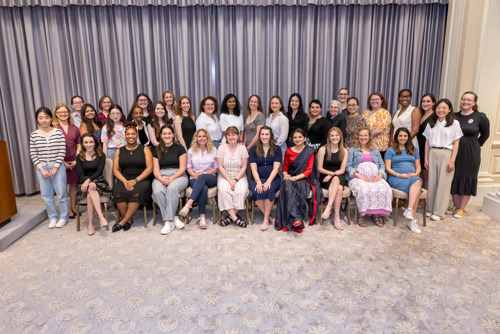 Photo: A group picture of the BU Women's Guild. There is a row of members sitting in the front of the picture and another row of members standing behind them