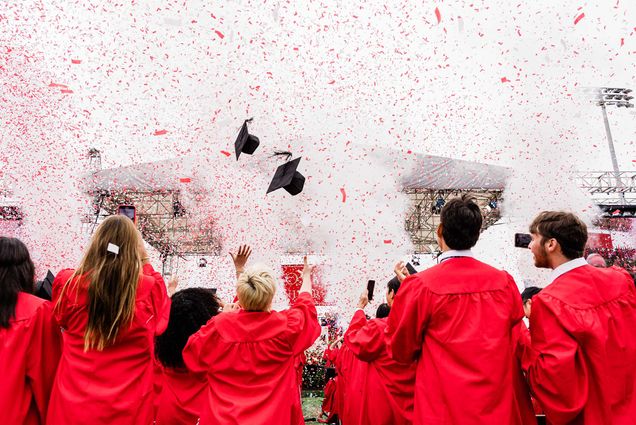Photo: A large group of graduating seniors in red robes at Boston University's commencement toss their mortarboards into the sky