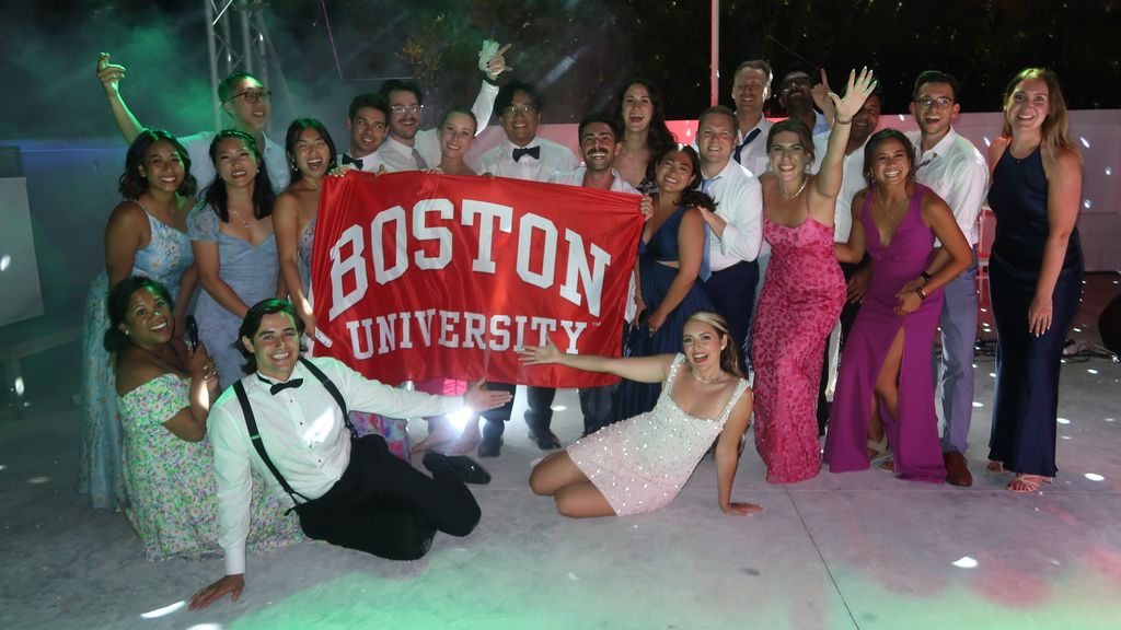 Photo: A group of people in dresses and suits holding a red "Boston University" banner at what appears to be a wedding
