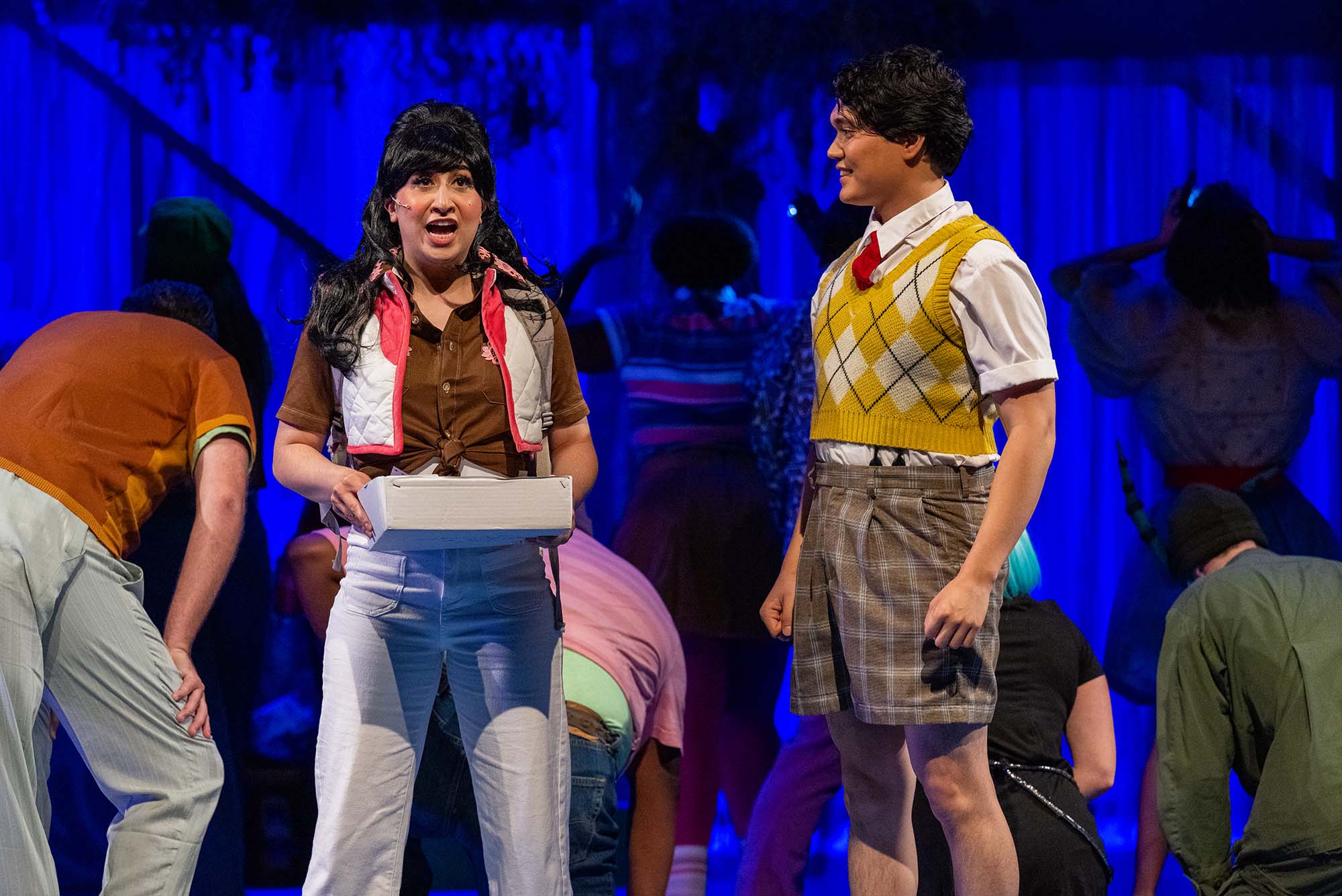 Photo: Two actors onstage at the Wheelock Family Theater performance of "Spongebob the Musical." On the left is an actress playing Sandy Cheeks, a squirrel. She has big hair, a brown shirt tied at the front, and a pink quilted vest. On the right is an actor playing Spongebob wearing a yellow sweater vest with a white short sleeve, collared shirt underneath.