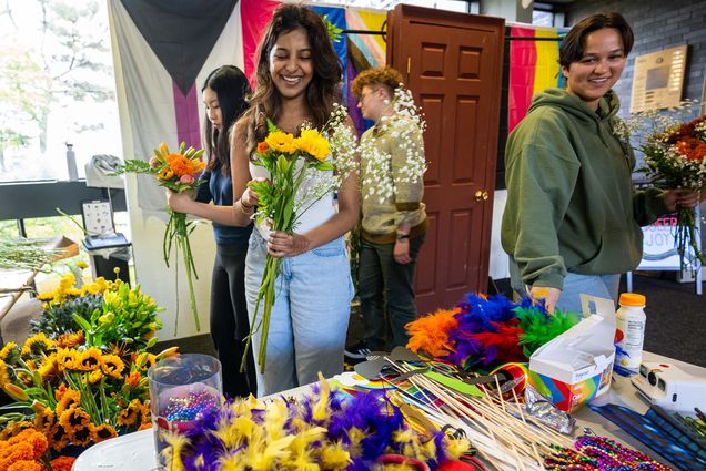 Photo: Students making bouquets of flowers at a station with various LGBTQIA+ flags behind them
