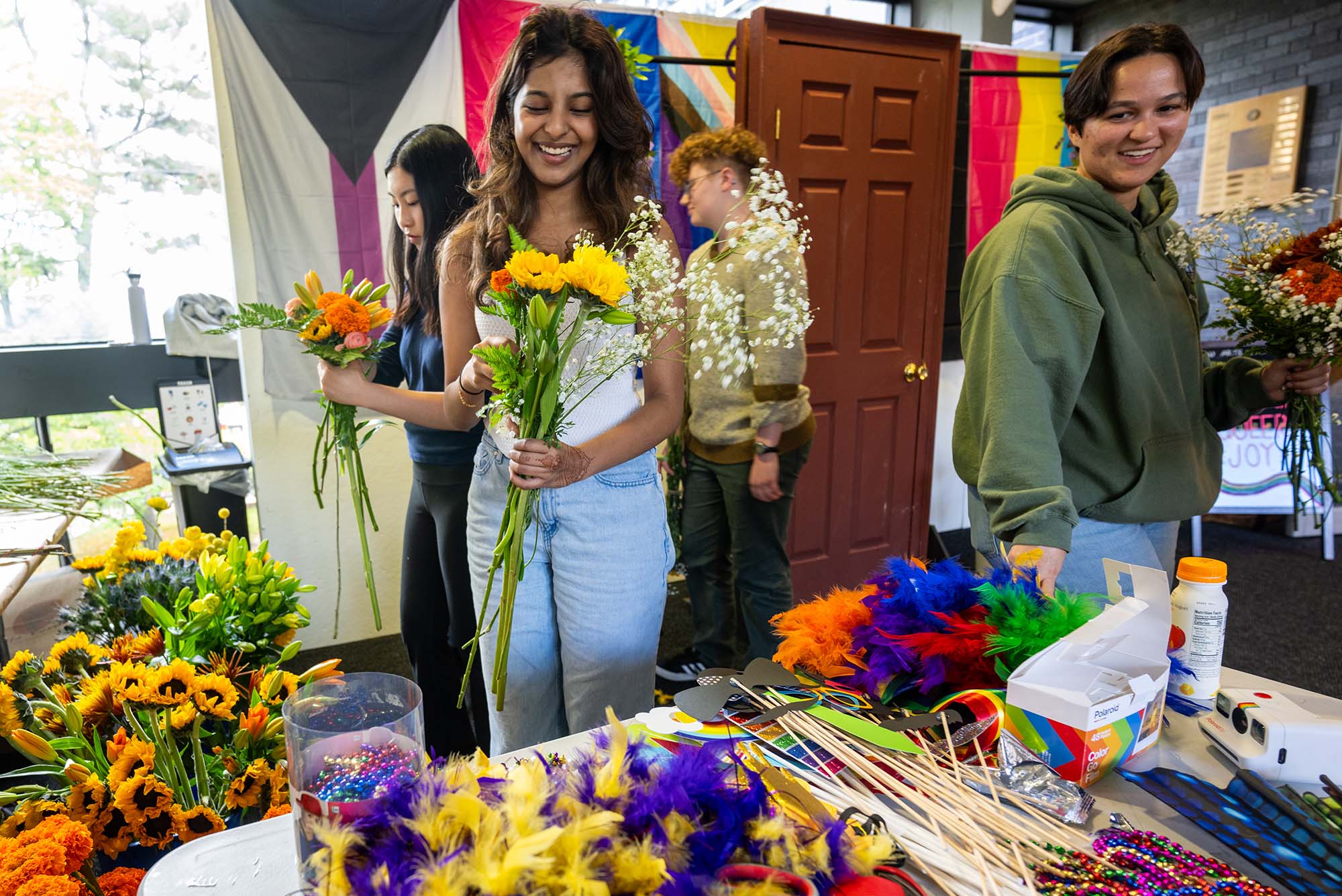 Photo: Students making bouquets of flowers at a station with various LGBTQIA+ flags behind them