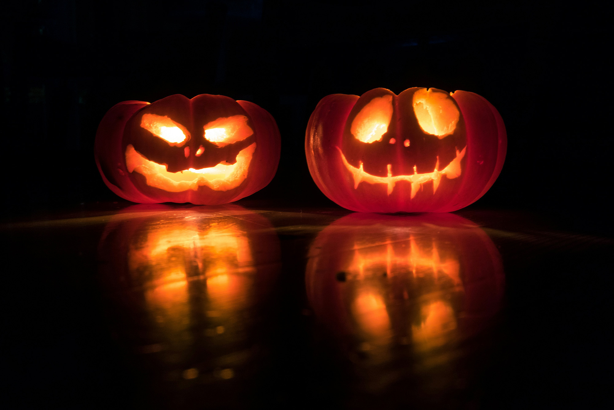 Photo: Two Jack-o-lanterns with creepy, smiling faces sit next to each other, glowing from the inside.
