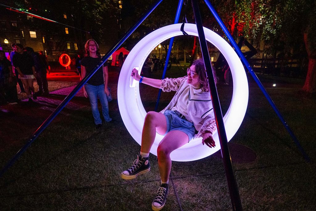 Photo: A student sitting on a light swing at nighttime during Boston University's Night of Lights