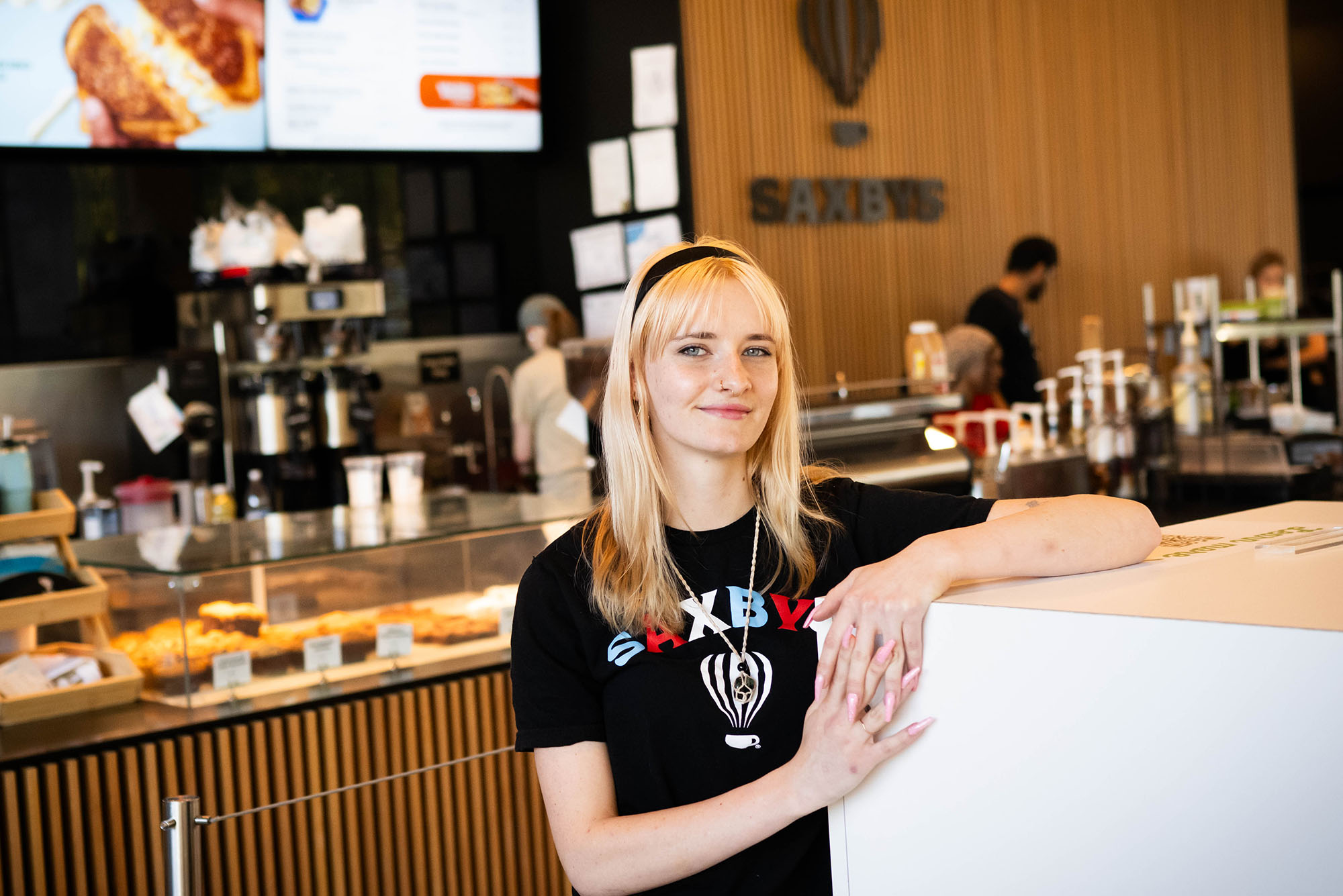 Photo: A blonde college student standing with fingers interlocked in front of a coffee counter