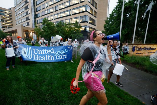 Photo: A protest against United Healthcare featuring a woman yelling into a megaphone and people holding a blue banner that says "United Denies Healthcare"