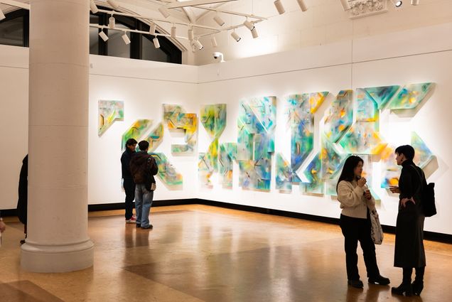 Photo: A display at an art gallery with bright greens, blues, and oranges in a piece that is split into many parts