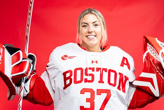 Photo: BU Women's hockey Goaltender Callie Shanahan poses for a headshot in full gear in front of a red background