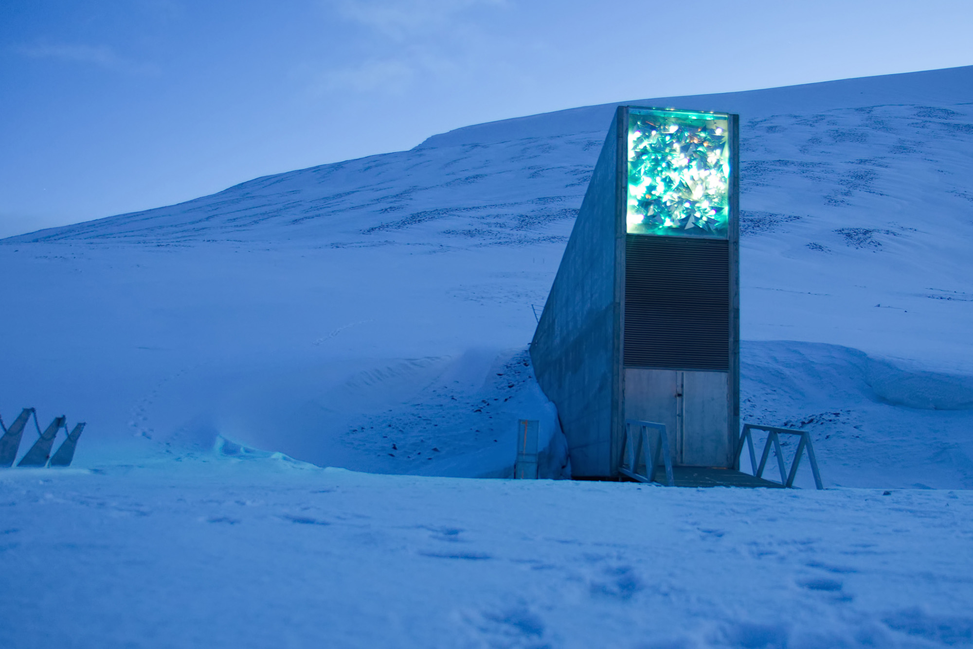 Photo: An exterior shot of the Svalbard Global Seed Vault. The building is peeking out of from a snowy mountain