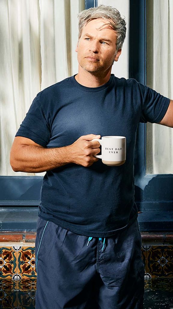 Photo: A man with gray hair wearing a blue tshirt, holding a coffee mug, and standing inside a fountain