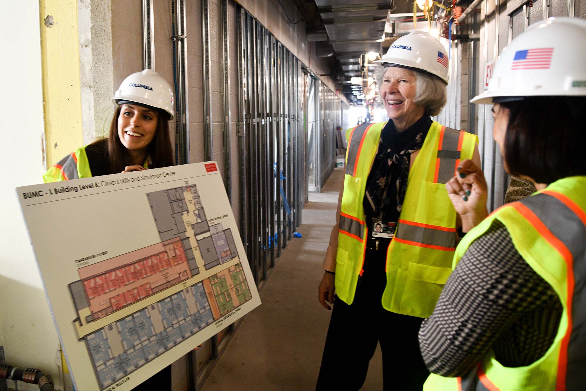 Photo: Three women in hi-vis vests and wearig construction hats review a large floorplan on a construction site