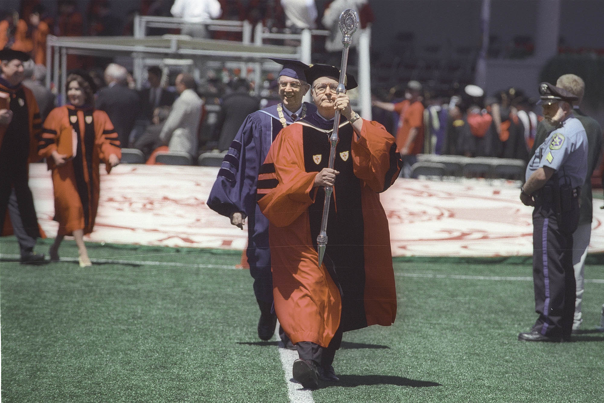Photo: An older gentleman in graduate regalia marches with Mace at Boston University's Commencement ceremony.
