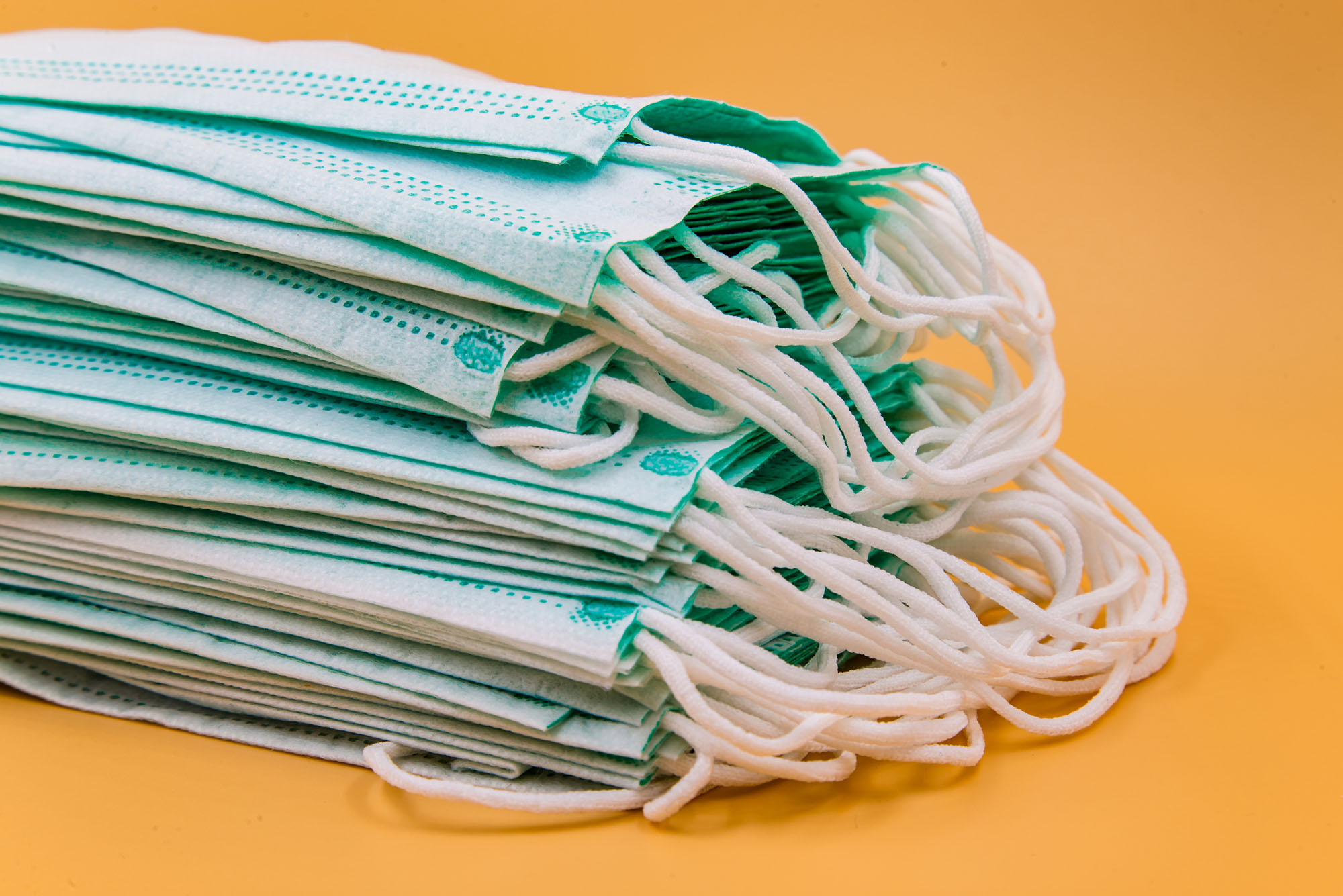 Photo: Blue disposable surgical masks in front of an orange background