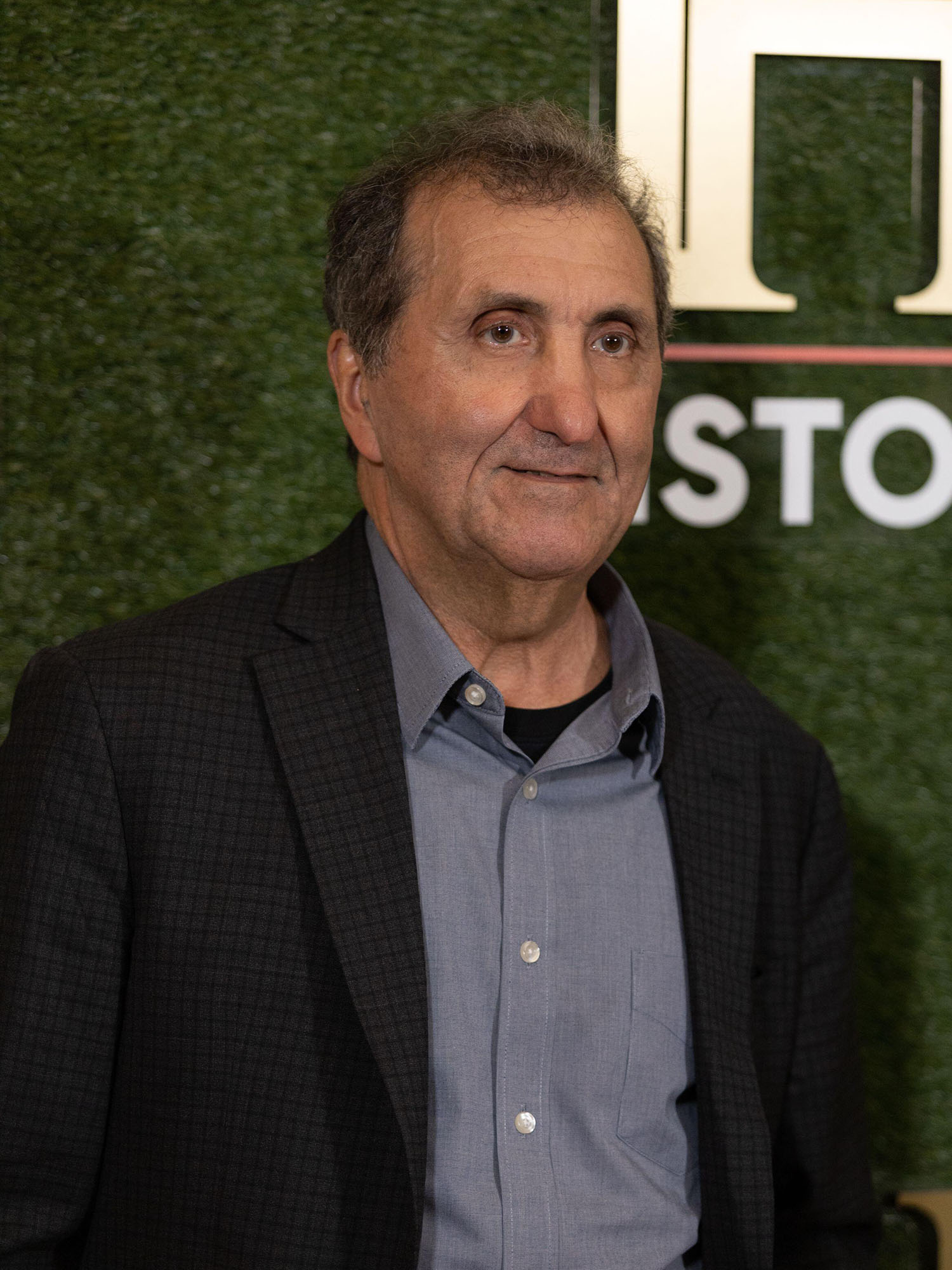 Photo: A white-passing man who is middle-aged in a black blazer and blue button up shirt.