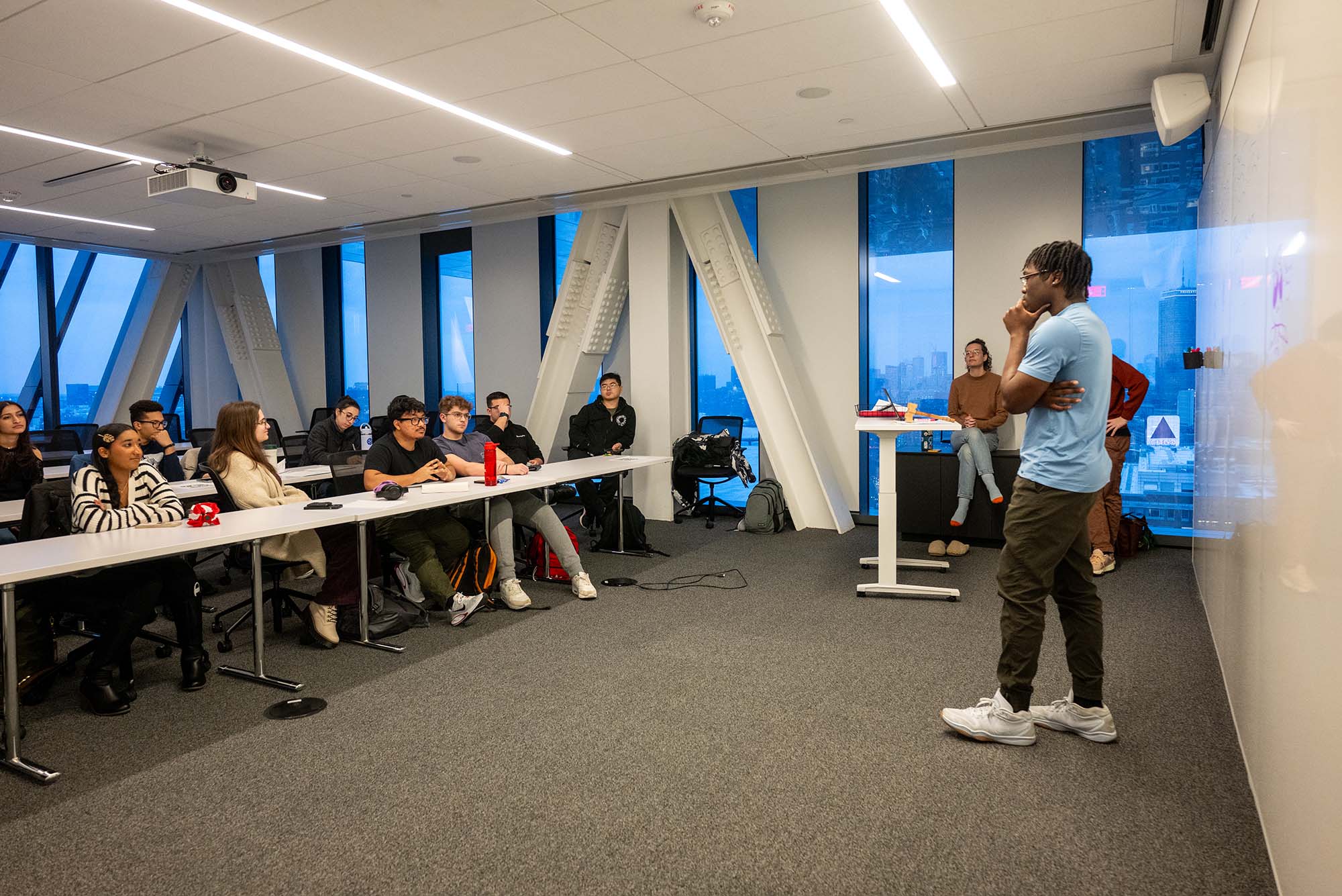 photo: A male student standing in front of a group of students at a public speaking club meeting