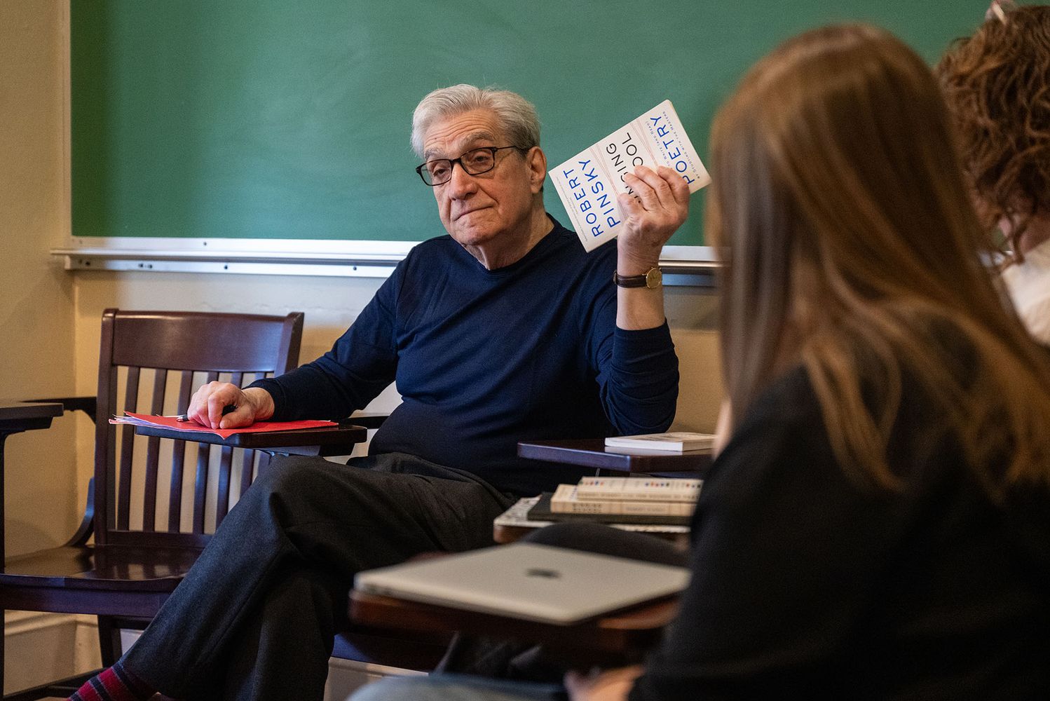Photo: Robert Pinsky holding up a book of his own poetry in a classroom of students