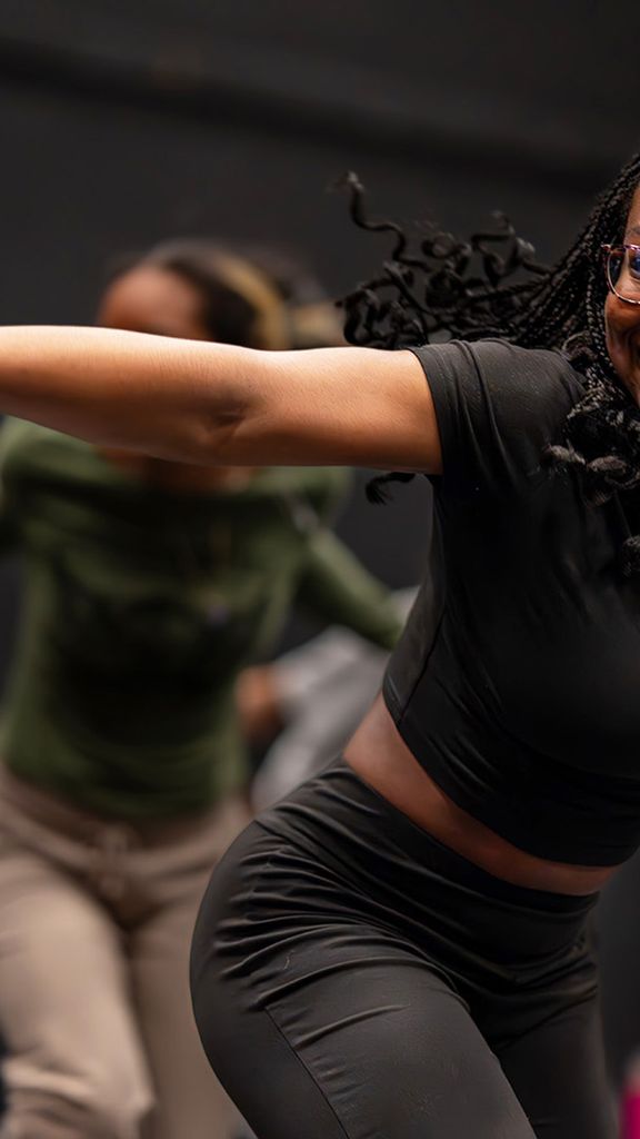 Photo: A woman in the foreground dancing with a few other people in the background. Her arm is extended and she is smiling