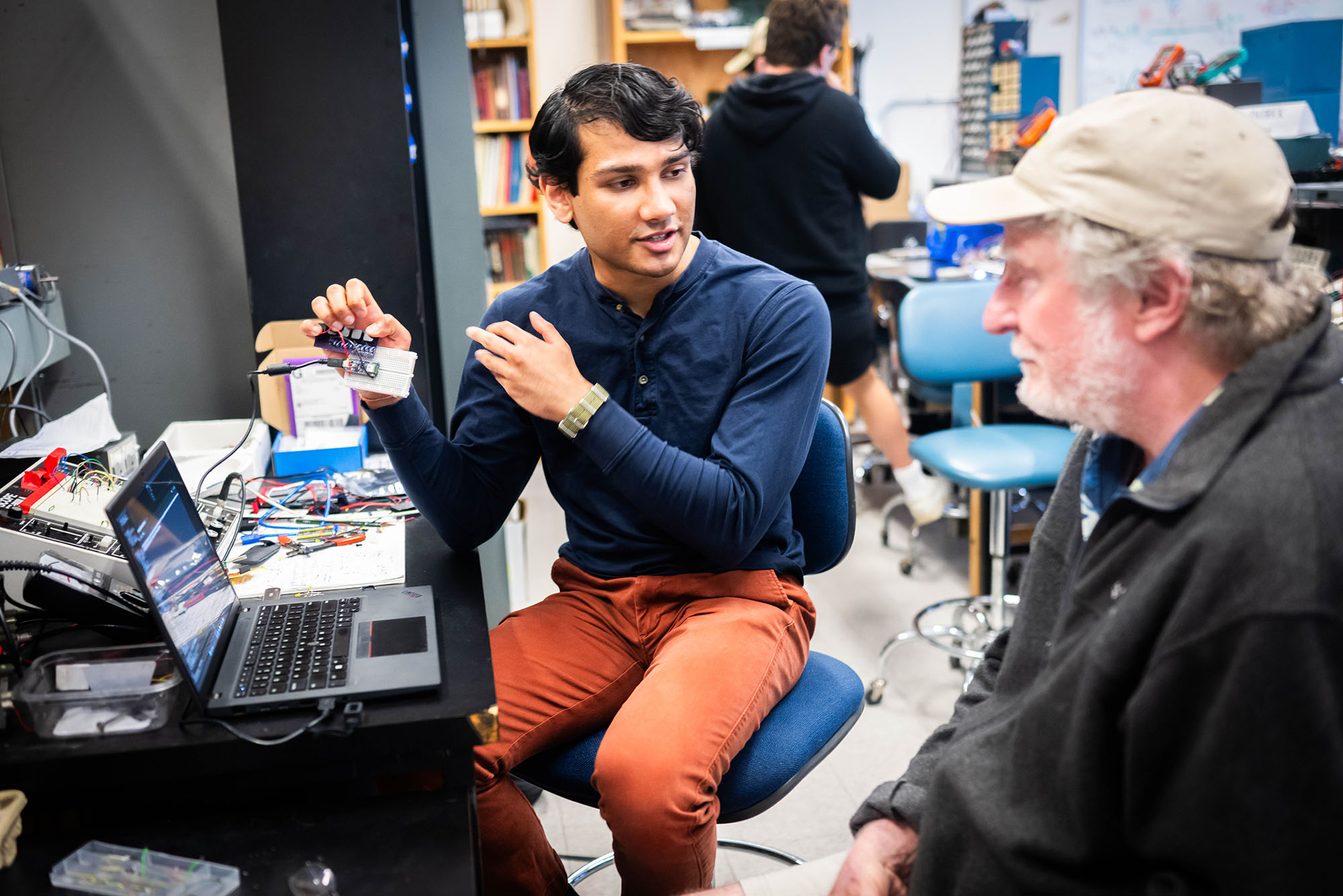 Phoot: A student presenting his project to a man next to him while they sit in the lab