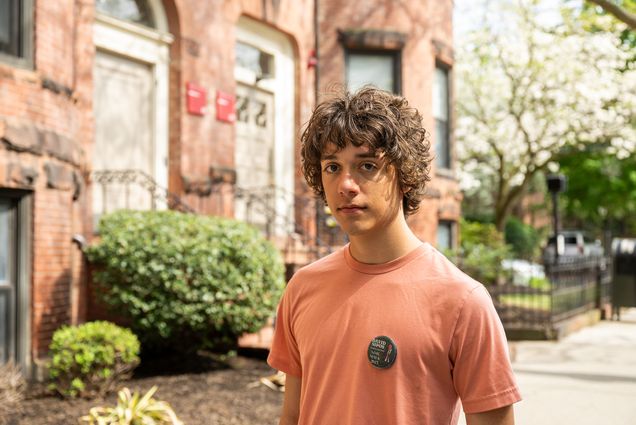 Photo: A male BU studentwith curly brown hair posing in a peach-colored shirt in front of a BU building