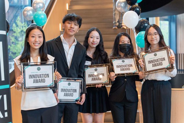 Photo: A group of students in formal attire smile for a photo, each with a certificate of their win.